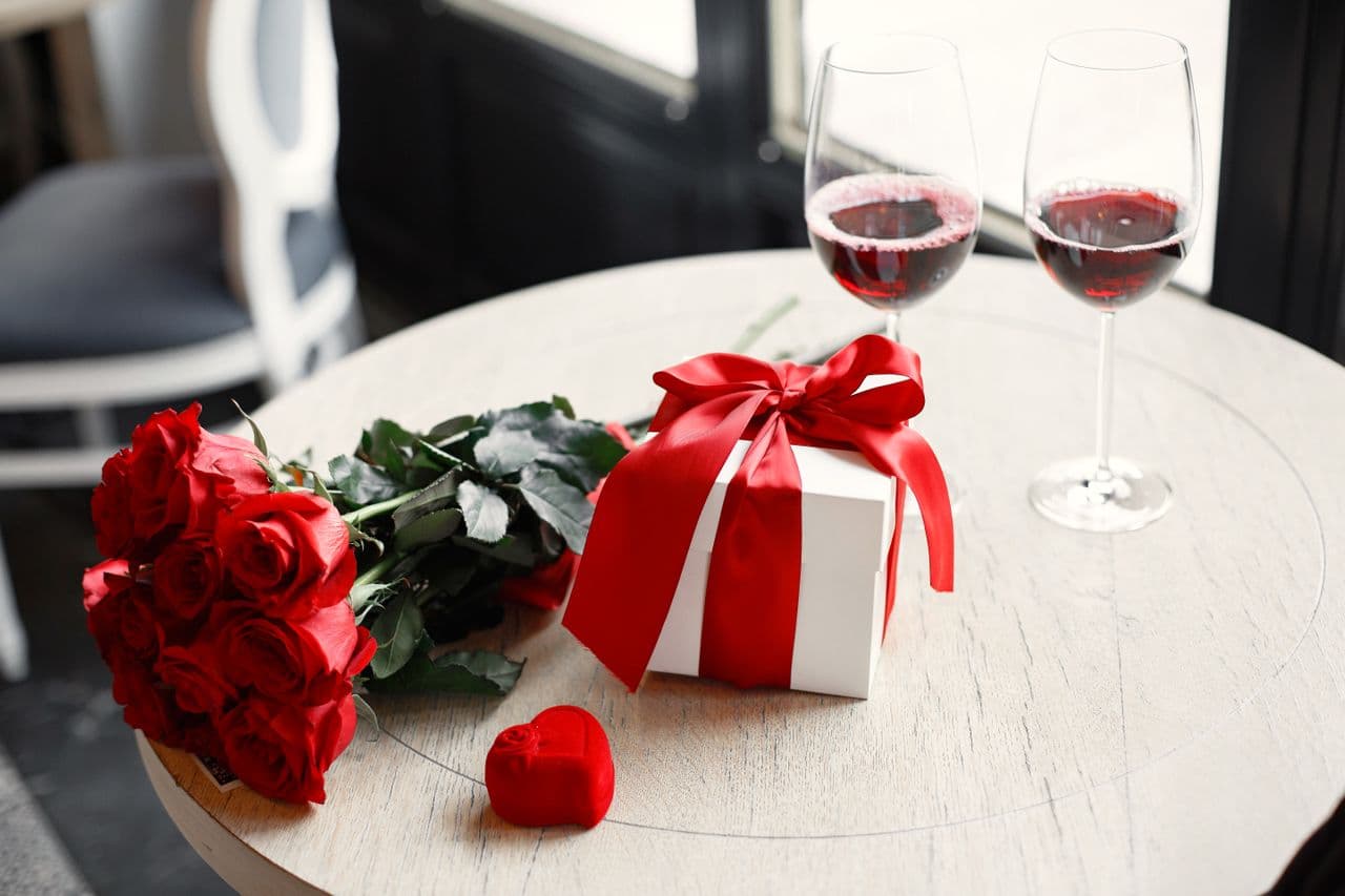 Röda rosor, en inslagen present och två glas rött vin på ett dukat bord